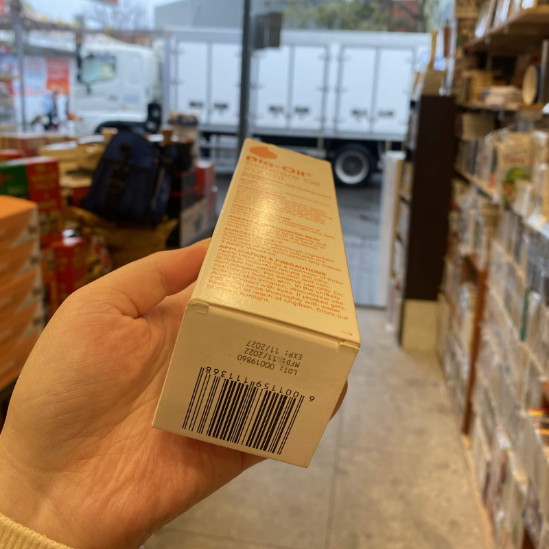 A hand holds a beige box of 'The Art of Eating' in a retail store aisle, with shelves and a white truck visible in the blurred background.