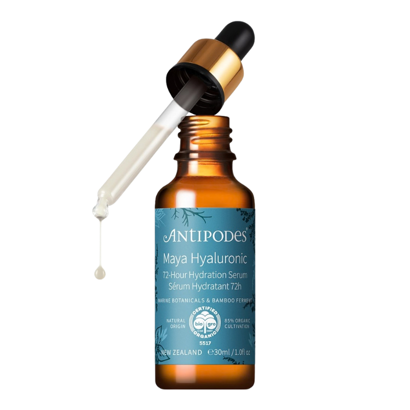 An amber glass dropper bottle of AntiPodes Maya Hyaluronic 12-hour hydration serum with a blue label, shown with the dropper tilted and a single drop of serum hanging from the tip against a white background.