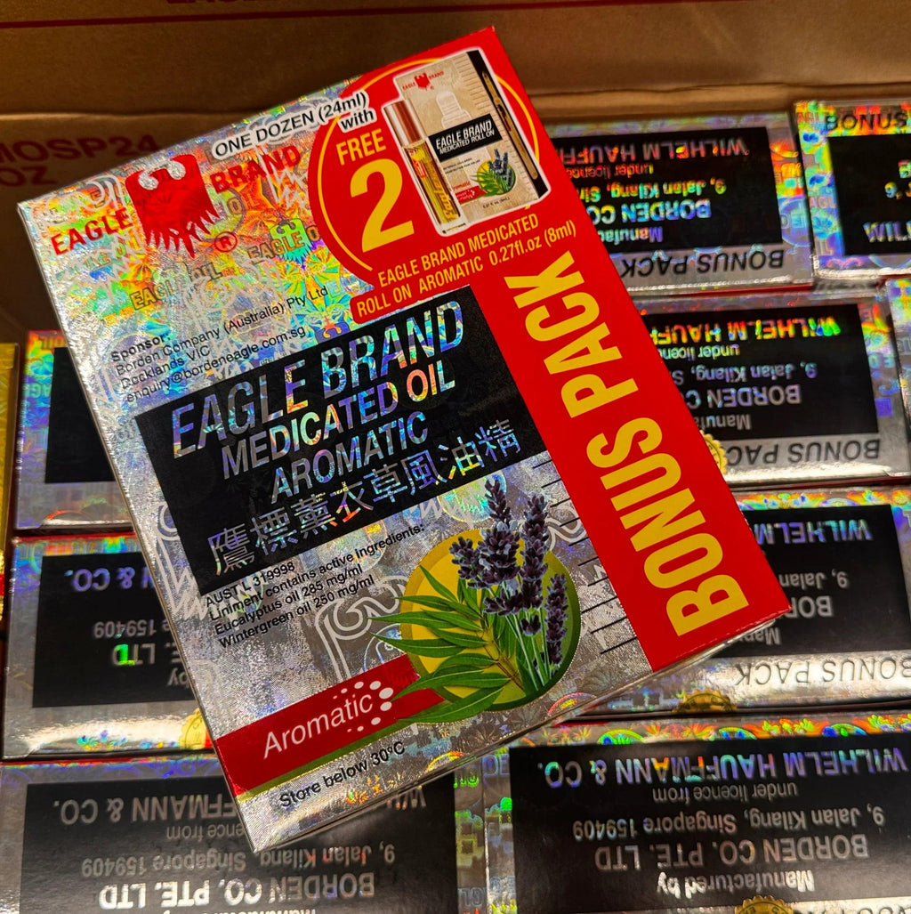 A box of Eagle Brand Aromatic Medicated Oil, featuring a red and black label with lavender illustrations, displayed on top of other identical boxes inside a cardboard shipping box.