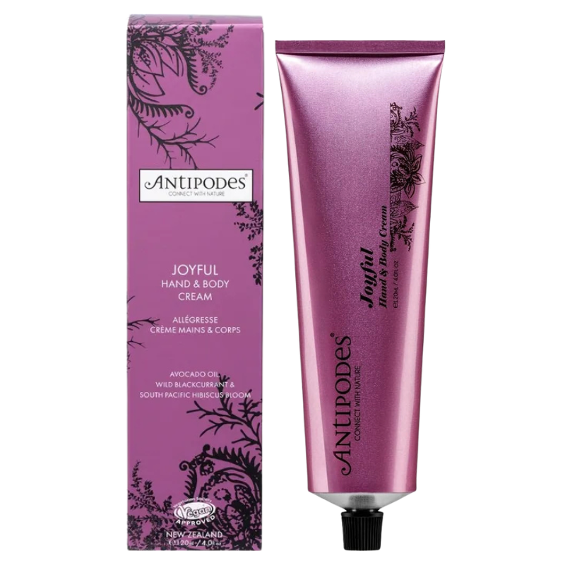 Antipodes Joyful Hand & Body Cream shown in a metallic pink squeeze tube next to its matching pink packaging box, on a plain white background.